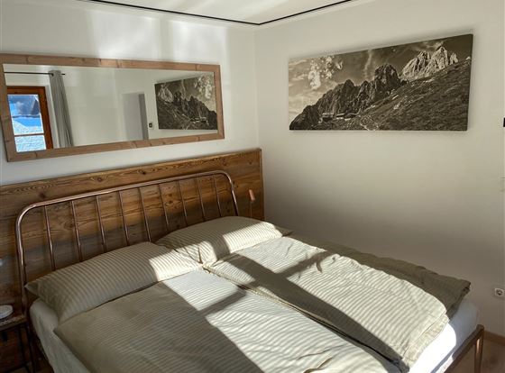 Ein gemütliches Schlafzimmer mit einem Doppelbett und gestreiften Bettdecken. An der Wand hängt ein großes Schwarz-Weiß-Bild der Berge.