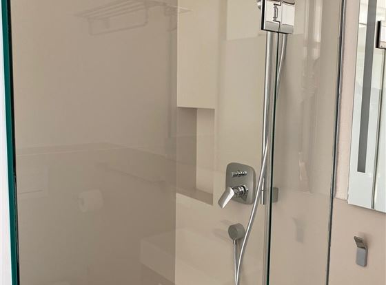 Eine moderne Duschkabine mit gläserner Trennwand und einem Handbrausekopf. Die Wände sind hell und schlicht gestaltet.