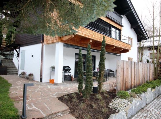 Ein modernes Haus mit einem großzügigen Balkon und einer gemütlichen Terrasse. Der Garten ist gepflegt und mit Steinen und Pflanzen gestaltet.