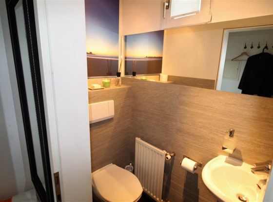 Ein modernes Badezimmer mit einer Toilette und einem Waschbecken. Die Wände sind mit grauen Fliesen und einem Landschaftsbild dekoriert.