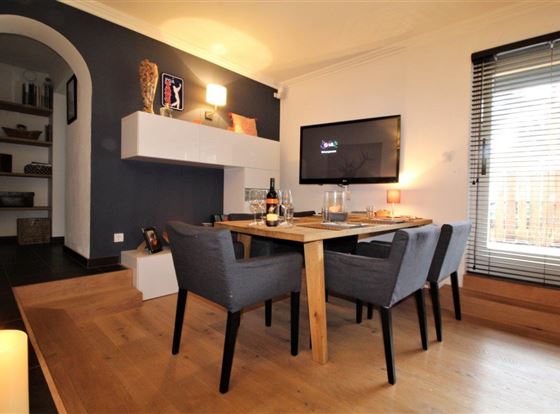 Ein moderner Essbereich mit einem Holztisch und gemütlichen Stühlen. An der Wand hängt ein Fernseher und es gibt eine angenehme Beleuchtung.