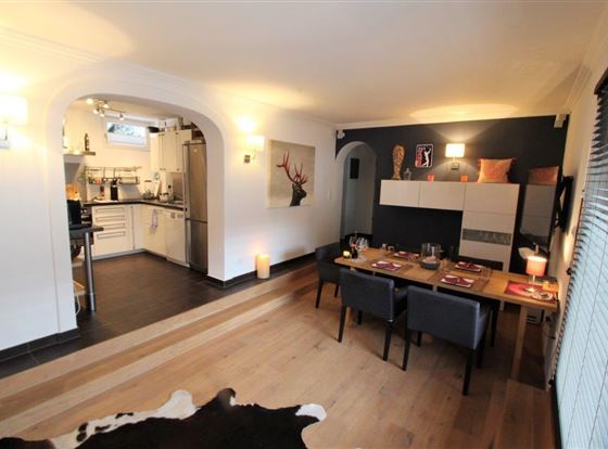Ein modernes Wohnzimmer mit einem Essbereich und einer offenen Küche. Der Raum ist hell und freundlich, mit Holzfußboden und eleganter Einrichtung.