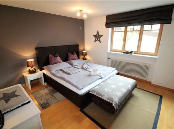 Ein gemütliches Schlafzimmer mit einem großen Bett und dekorativen Kissen. Helle Wände und ein Fenster sorgen für eine freundliche Atmosphäre.