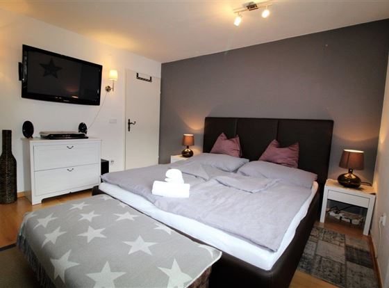 Ein stilvolles Schlafzimmer mit einem großen Doppelbett und gemütlichen Kissen. Die Wände sind in neutralen Tönen gehalten, und es gibt modernes Licht und Dekorationen.