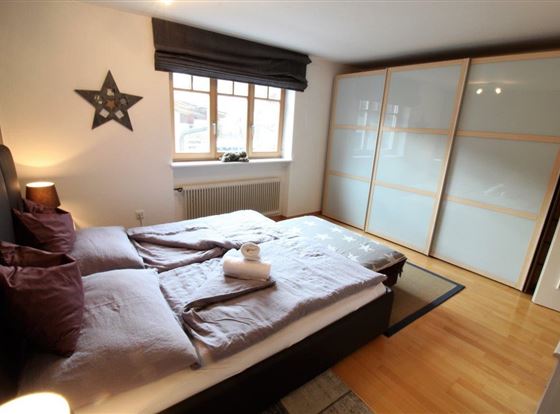 Ein gemütliches Schlafzimmer mit einem Doppelbett und zwei Kissen. Der Raum hat große Fenster und moderne Möbel, die eine helle und einladende Atmosphäre schaffen.