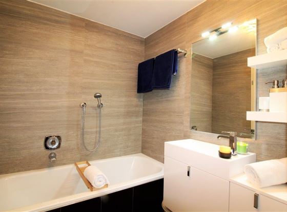 Ein modernes Badezimmer mit einer Badewanne und einer eleganten Waschbecken-Anlage. Die Wände sind in warmen Farbtönen gestaltet und es sind Handtücher und Toilettenartikel sichtbar.