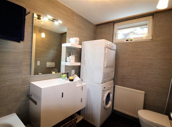 Ein modernes Badezimmer mit einer Waschmaschine, einem Spiegel und einem schlichten Waschbecken. Die Wände sind in neutralen Tönen gehalten, was einen eleganten Look erzeugt.