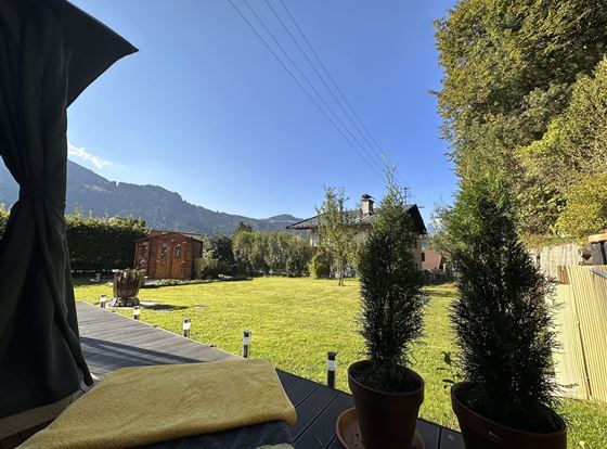 Ein schöner Garten mit grünem Rasen und Bäumen. Im Hintergrund sind Berge und ein strahlend blauer Himmel sichtbar.