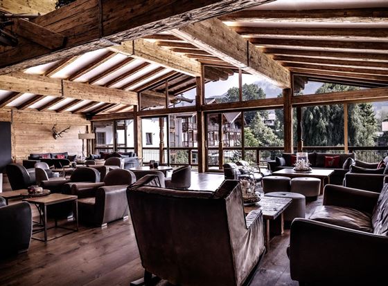 Ein gemütliches Lounge-Ambiente mit Holzdecke und großen Fenstern. Die Einrichtung besteht aus bequemen Sesseln und einem einladenden Tisch.