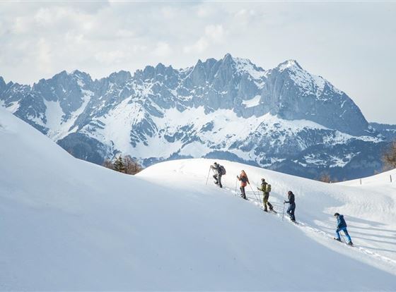 Eine Gruppe von Menschen beim Skifahren in schneebedeckten Bergen. Im Hintergrund sind beeindruckende Felsformationen sichtbar.