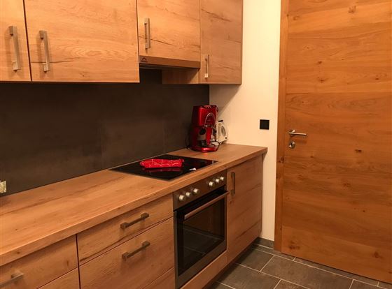 Eine moderne Küche mit Holzmöbeln und eleganten Geräten. Es gibt einen Herd, einen Backofen und eine Kaffeemaschine in einem gut gestalteten Raum.