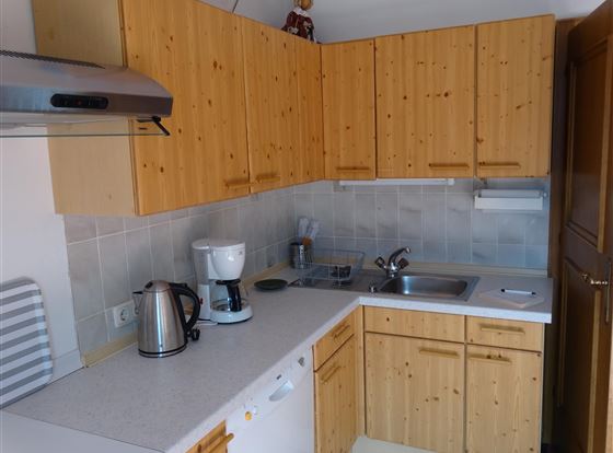 Eine moderne Küche mit Holzschränken und einer hellen Arbeitsfläche. Sie enthält grundlegende Geräte wie einen Wasserkocher und eine Kaffeemaschine.