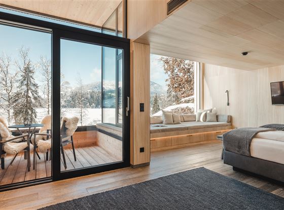 Ein modernes Zimmer mit Holzdekor und großen Fenstern. Draußen sieht man eine winterliche Berglandschaft.