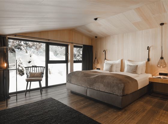 Ein modernes Schlafzimmer mit Holzverkleidung und großen Fenstern. Der Blick zeigt verschneite Landschaften und eine gemütliche Einrichtung.