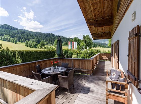 Ein schöner Balkon mit Blick auf die grünen Hügel. Ein Tisch mit Stühlen lädt zum Entspannen ein.