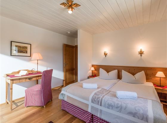 Ein gemütliches Schlafzimmer mit zwei Betten und einem Schreibtisch. Warmes Licht und Holzdetails schaffen eine einladende Atmosphäre.