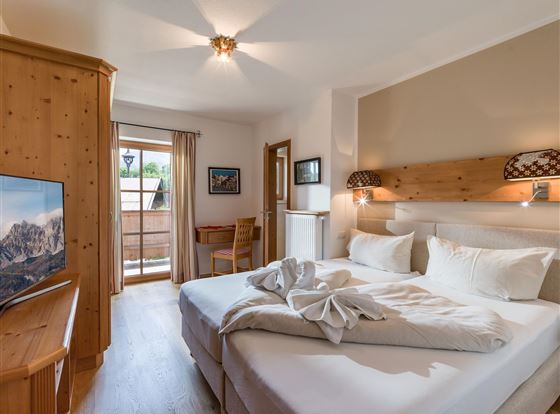 Ein gemütliches Schlafzimmer mit zwei Betten und Holzverkleidung. Ein Fernseher und ein Balkon mit Blick nach draußen sind ebenfalls vorhanden.
