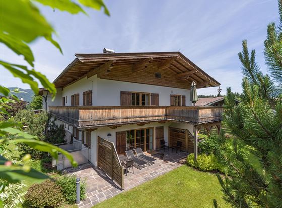 Ein schönes Haus mit einem Balkon und einem gepflegten Garten. Umgeben von Bäumen und grüner Landschaft.