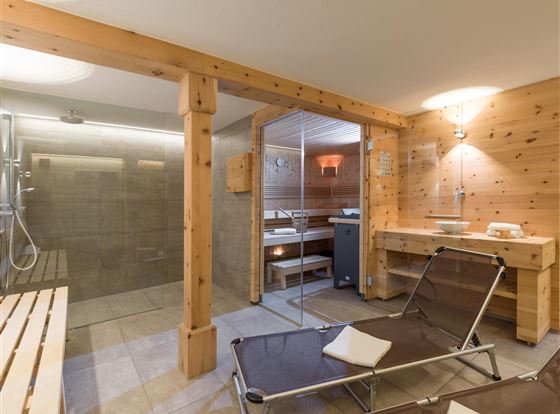Ein moderner Wellnessbereich mit einer Sauna und einer Dusche. Holzverkleidungen und entspannende Liegen sorgen für eine gemütliche Atmosphäre.