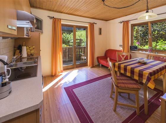 Eine gemütliche Küche mit einem Esstisch und schönen Stühlen. Große Fenster lassen viel Licht herein und bieten einen Blick auf den Garten.