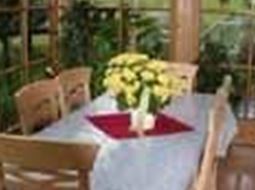 Ein helles Esszimmer mit einer Holztisch und Stühlen. Auf dem Tisch steht ein Strauß gelber Blumen.