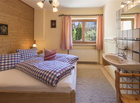 Ein gemütliches Schlafzimmer mit einem Doppelbett und karierten Bettdecken. Die große Fensterfront bietet einen Blick auf die Natur.