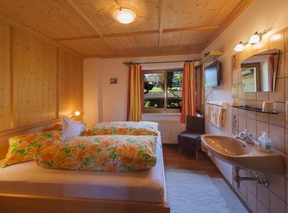 Ein gemütliches Schlafzimmer mit zwei Betten und bunten Bettdecken. Die Wände sind aus Holz, und es gibt ein Fenster mit Blick ins Grüne.