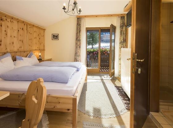 Ein gemütliches Zimmer mit einem Doppelbett und hellen Kissen. Der Raum hat einen Zugang zu einem Balkon mit Blick auf die Natur.