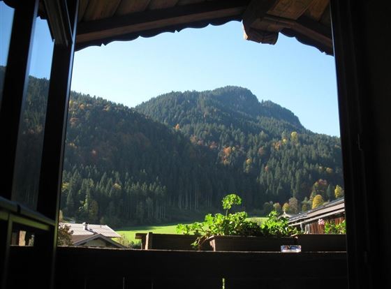 Blick aus einem Fenster auf majestätische Berge und dichte Wälder im Herbst. Der klare Himmel und die bunten Blätter schaffen eine ruhige Atmosphäre.