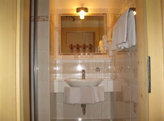 Ein Badezimmer mit einem Waschbecken, einem großen Spiegel und Handtüchern. Die Wände sind hell gefliest und es gibt eine angenehme Beleuchtung.