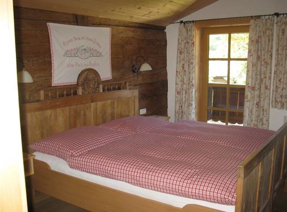 Ein gemütliches Schlafzimmer mit einem Holzbett und karierten Bettdecken. Große Fenster lassen viel Licht herein und bieten einen Blick auf die Natur.