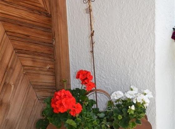 Ein Pflanzengefäß aus Metall mit roten und weißen Blumen steht an der Wand. Darüber befindet sich ein herzförmiges Schild mit der Aufschrift „Willkommen“.