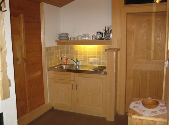 Eine kleine, gemütliche Küche aus Holz mit einer Spüle und Kochplatte. Die Wände sind hell gehalten und es gibt einfache Küchenutensilien.