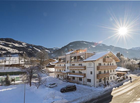 Ein modernes Gebäude in einer verschneiten Landschaft. Die Sonne scheint über den Bergen und dem klaren blauen Himmel.