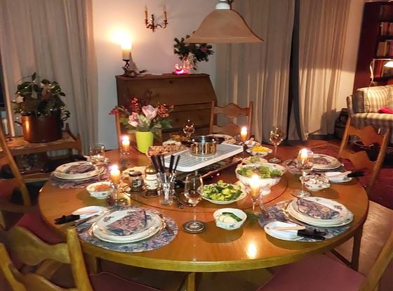 Ein gemütlicher Esstisch mit mehreren Gedecken und Kerzenlicht. Die Atmosphäre ist warm und einladend, ideal für ein Dinner mit Freunden oder Familie.