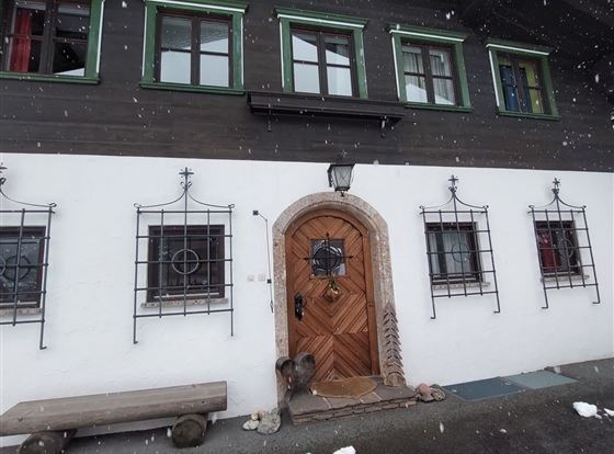Ein traditionelles Haus mit einem Holztür und großen Fenstern. Es liegt in einer verschneiten Umgebung.