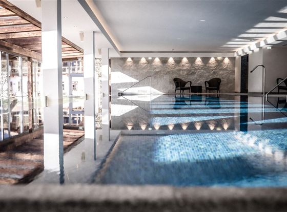 Ein eleganter Innenpool mit Glaswänden und stilvollen Holzdetails. Zwei Stühle stehen am Beckenrand in einer ruhigen Atmosphäre.