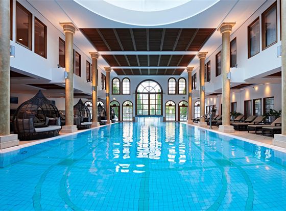 An elegant indoor pool with clear, blue water and stylish columns. The large window front lets in plenty of daylight and creates a relaxing atmosphere.