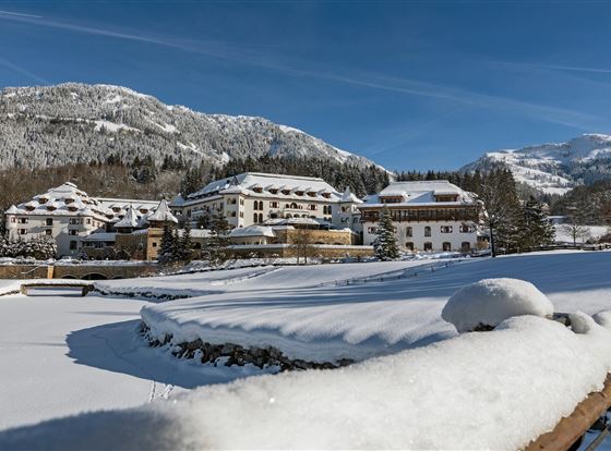 Eine Winterlandschaft mit schneebedeckten Bergen und einem Hotel. Der Himmel ist klar und blau, was einen schönen Kontrast zur weißen Schneedecke bildet.