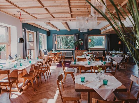 Ein gemütliches Restaurant mit Holzdekor und großen Fenstern. Tische sind mit grünen Gläsern und Blumen dekoriert.