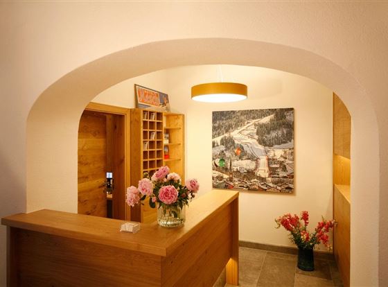 Ein gemütlicher Empfangsbereich mit einem Holzschalter und frischen Blumen. An der Wand hängt ein farbenfrohes Gemälde einer Landschaft.