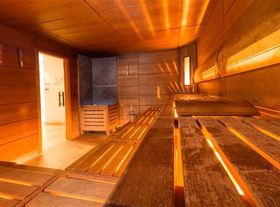 Eine gemütliche Sauna mit Holzverkleidung und gedämpftem Licht. Die Bank zum Sitzen lädt zum Entspannen ein.