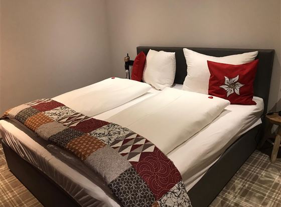 Ein gemütliches Schlafzimmer mit einem großen Doppelbett. Die Bettdecke hat ein farbenfrohes Design und es gibt dekorative Kissen.