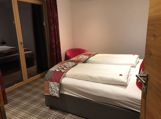 Ein gemütliches Zimmer mit einem großen Bett und einem modernen Dekor. Es gibt einen roten Sessel und große Fenster, die viel Licht hereinlassen.
