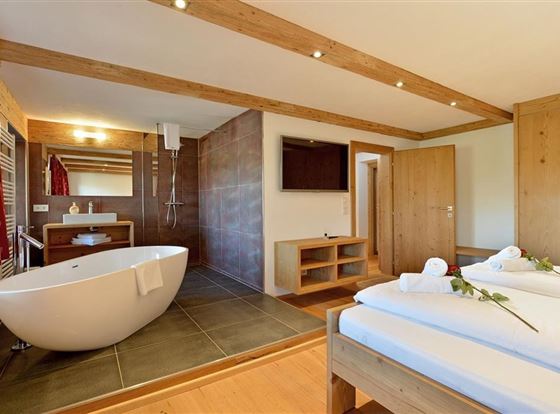 Ein modernes Zimmer mit einem gemütlichen Bett und einem eleganten Badezimmer. Die freistehende Badewanne und die warmen Holzelemente schaffen eine entspannte Atmosphäre.