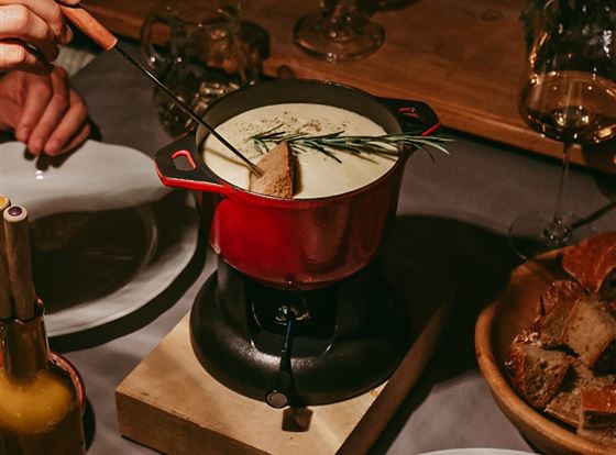 Ein gemütliches Abendessen mit Käsefondue in einem roten Topf. Umgeben von Brot, Salat und einem festlichen Ambiente.