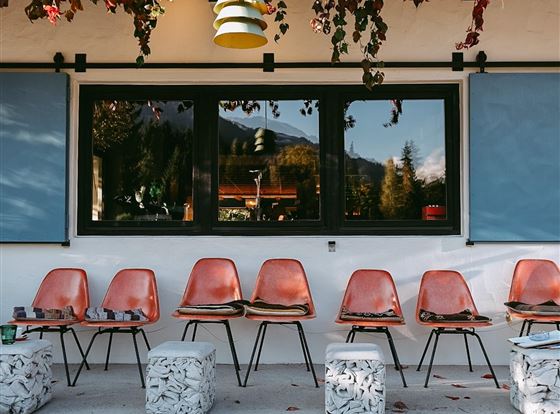 Ein gemütlicher Außenbereich mit mehreren Stühlen und Hockern. Bunte Blätter hängen über die Veranda und schaffen eine einladende Atmosphäre.
