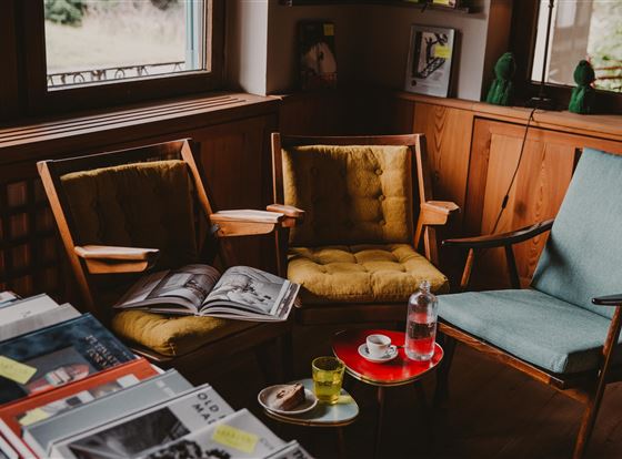 Gemütliche Sitzecke mit zwei Holzstühlen und einem kleinen Tisch. Auf dem Tisch stehen Getränke und Bücher.
