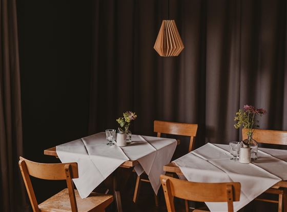 Ein gemütliches Restaurant mit Holztischen und Stühlen. Auf den Tischen stehen Blumenvasen und zeitlose Tischdecken.