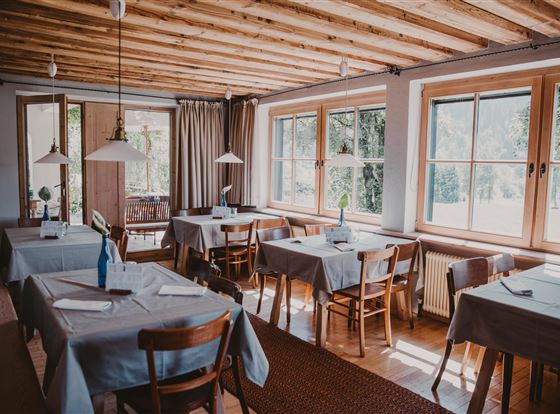 Ein gemütliches Restaurant mit Holzbalkendecke. Eingedeckte Tische und große Fenster bieten einen Blick auf die Landschaft.